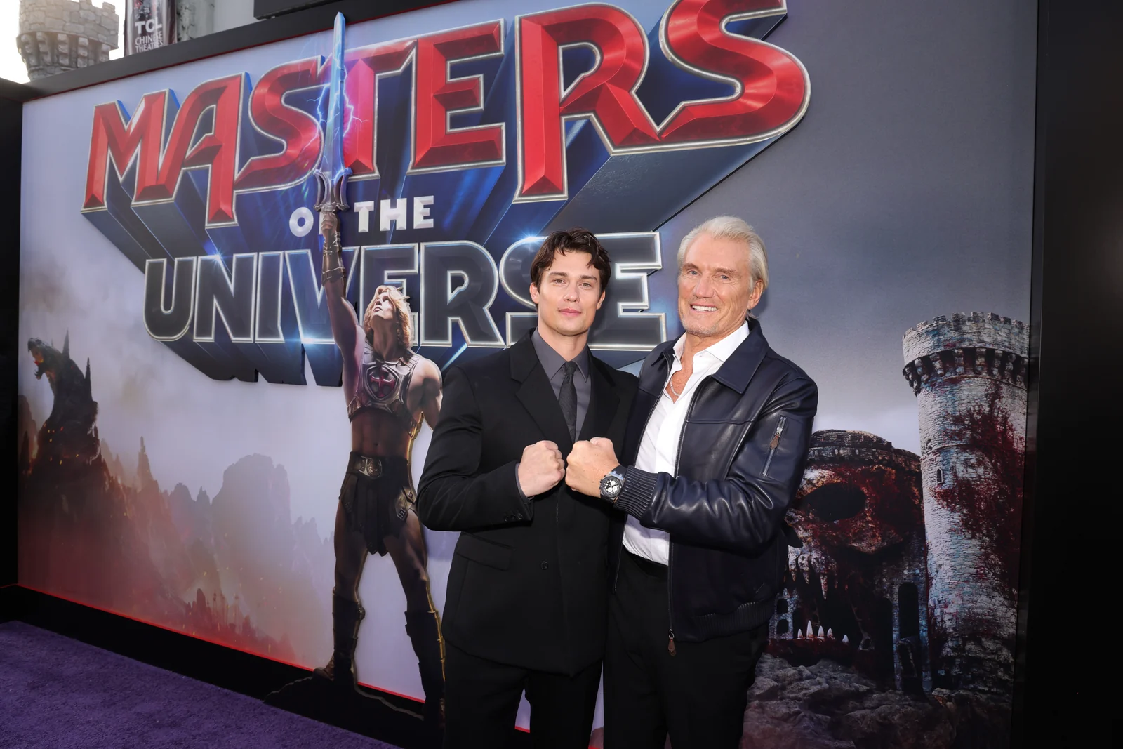Nicholas Galitzine and Dolph Lundgren pose fists-up in front of the Masters of the Universe poster at the world premiere