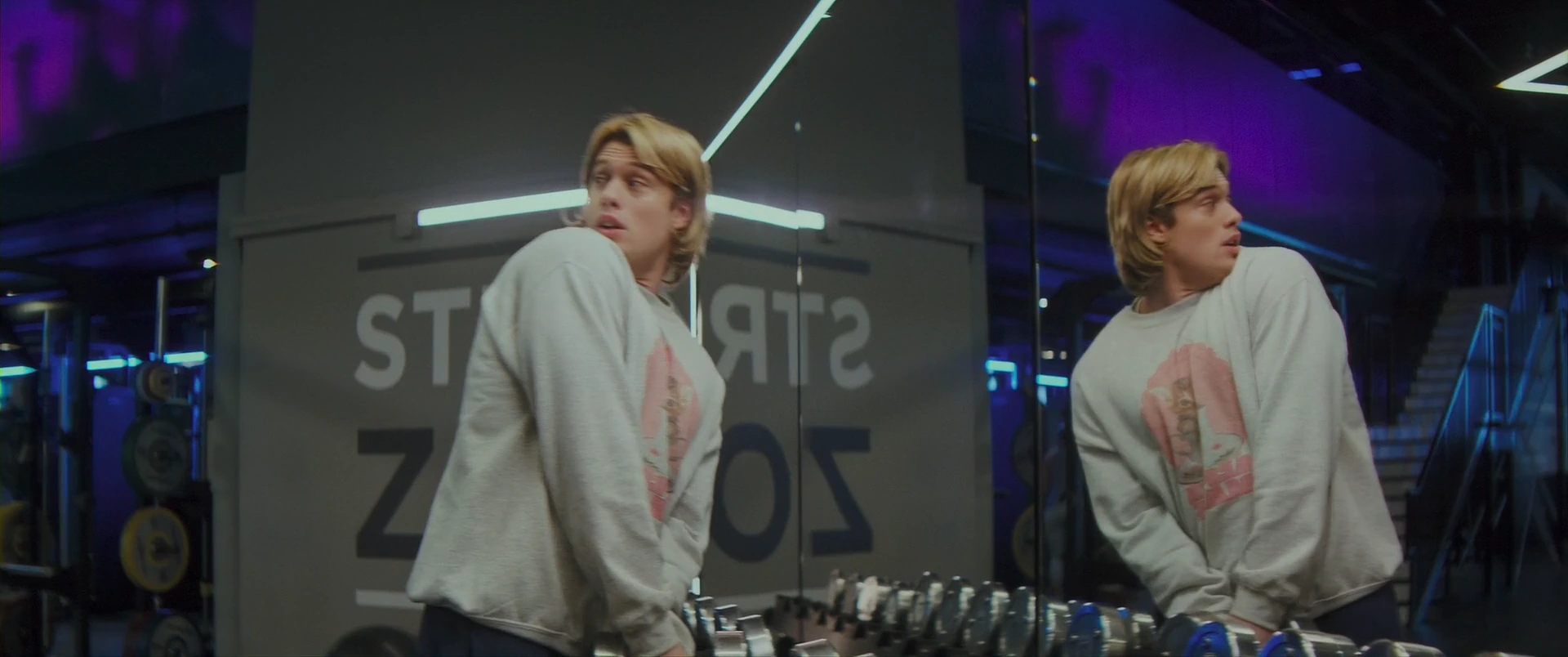 The sword’s pull catches Adam again, startled, before a gym mirror.