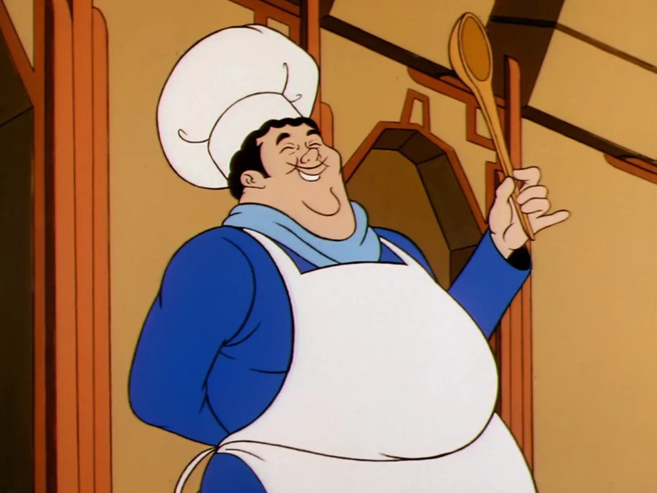 The palace chef laughs heartily while holding up his wooden spoon in a close up shot.