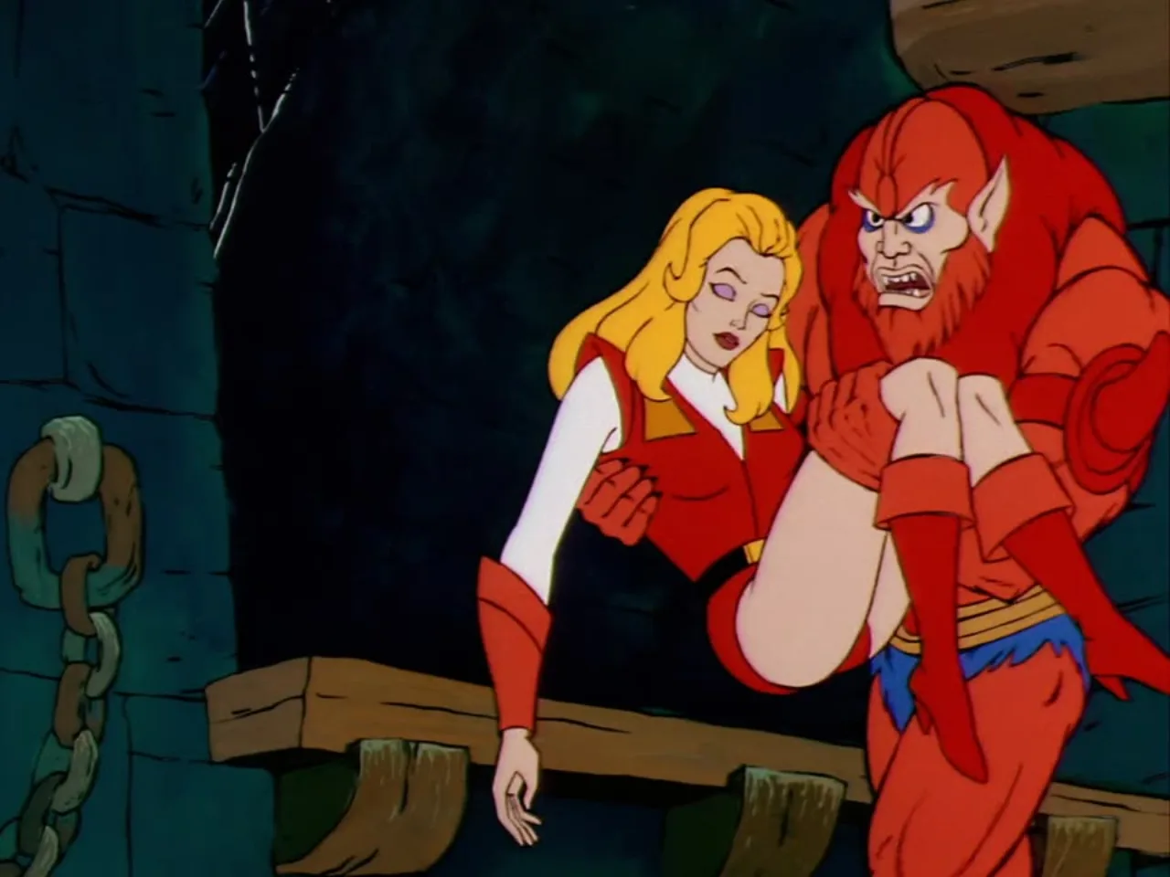 Beast Man carries the unconscious Adora in his arms past a heavy hanging chain inside a dungeon cell.