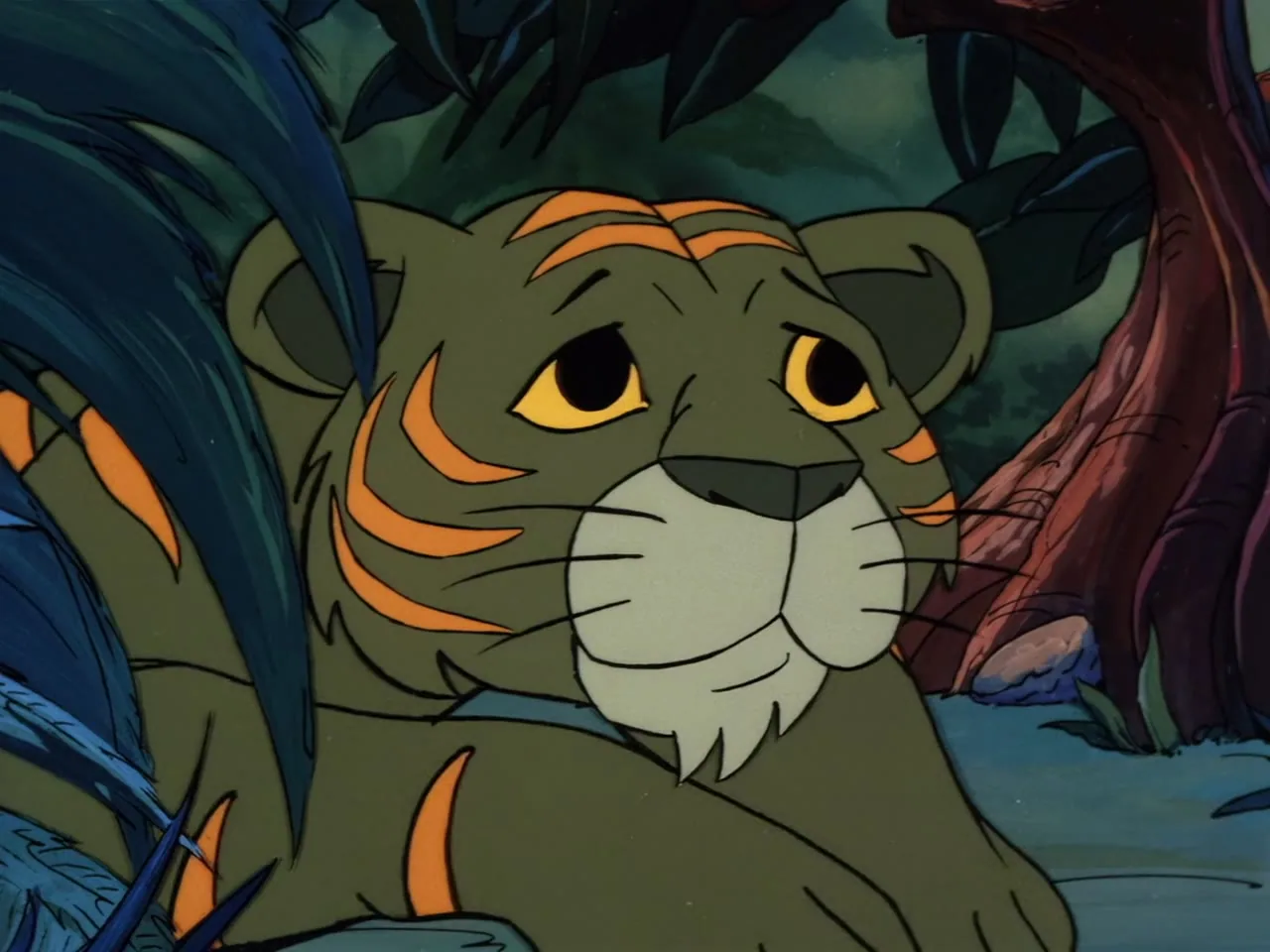 A small green tiger cub with orange stripes looks up, lying in the jungle.
