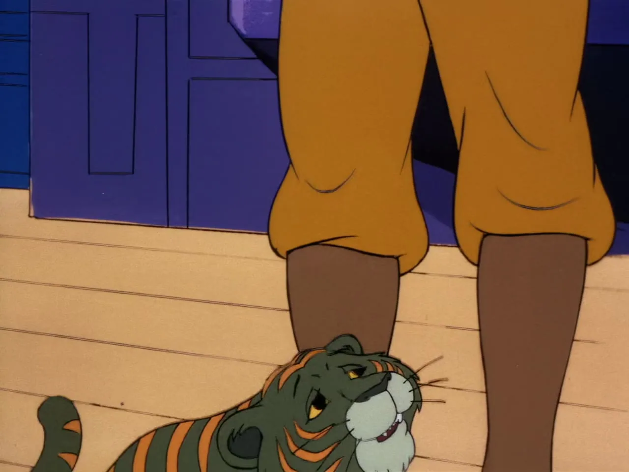 The small green tiger cub with orange stripes sits up, looking at a red food bowl held by a pale hand with white sleeve.