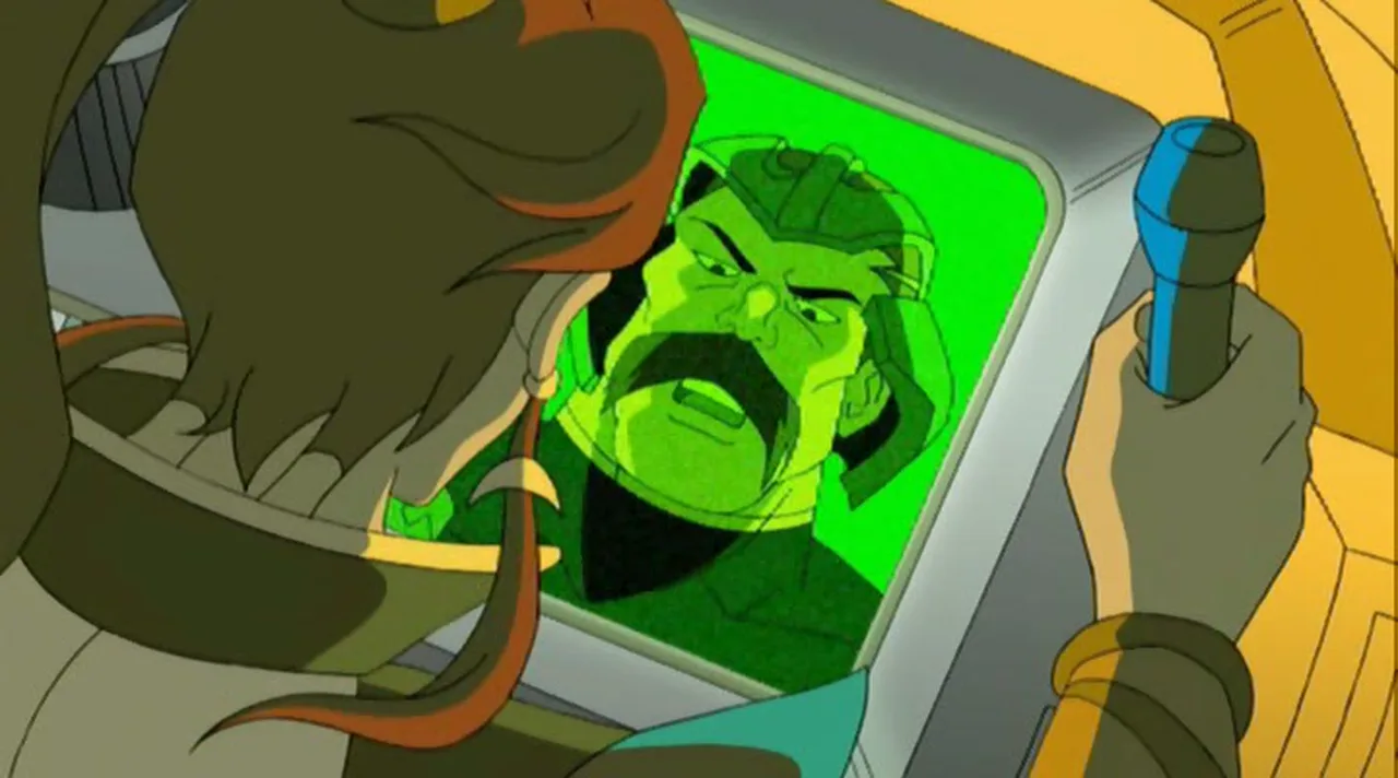 Man-At-Arms appears on a green screen as Teela listens.